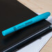 A Universal fluorescent blue pen on a black notebook.