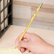 A hand holds a yellow Dixon Ticonderoga pencil in front of a box.