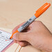 A person's hand using a Sharpie Orange Fine Point Permanent Marker to check a box.