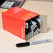 A box of Universal black bullet tip permanent markers with one pen on top.