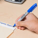 A person holding a Sharpie blue fine point permanent marker and writing on a piece of paper.