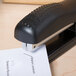 A Bostitch black ergonomic desktop stapler on a piece of paper.
