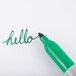 A close up of a Sharpie green fine point permanent marker writing in green on a white surface.