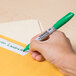 A hand using a green Sharpie to write on a yellow envelope.