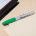 A green Sharpie fine point marker writes on a piece of paper.