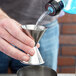 A hand using an American Metalcraft stainless steel jigger to pour a drink.