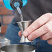 A hand using an American Metalcraft stainless steel Japanese jigger to pour liquid into a metal cup.