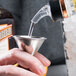 A person using an American Metalcraft stainless steel jigger to pour a shot.