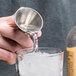 A hand using an American Metalcraft stainless steel jigger to pour liquid into a glass of ice.