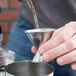 A person using an American Metalcraft stainless steel jigger to pour liquid.