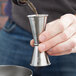 A person using an American Metalcraft stainless steel Japanese jigger to pour liquid.