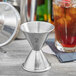An American Metalcraft stainless steel jigger with 1.25 and 2 oz. cups next to a glass of liquid.