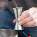 A person using an American Metalcraft stainless steel jigger to pour a shot.