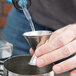 A hand using an American Metalcraft stainless steel jigger to pour liquid into a metal cup.