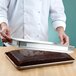 A person holding a Baker's Mark half-size sheet pan extender over a tray of chocolate cake.