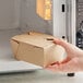 A hand holding a Choice Kraft paper take-out box in front of a microwave.