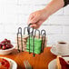 A hand holding a Tablecraft black wire jelly packet rack with a stack of napkins in it.