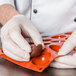 A person in white gloves uses a Matfer Bourgeat silicone mold to make chocolate half spheres.