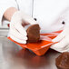 A gloved hand places a brown cake into a Matfer Bourgeat pyramid mold.