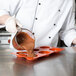 A person pouring brown liquid into a Matfer Bourgeat silicone savarin mold.