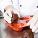 A person in white gloves putting a chocolate muffin into a Matfer Bourgeat orange silicone mold.