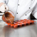 A chef pouring brown liquid into a Matfer Bourgeat orange silicone mold.