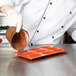 A chef pouring chocolate into an orange silicone Madeleine baking tray.