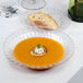 A Fineline clear plastic bowl filled with soup with a slice of bread on top.