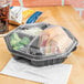 A Solo black plastic container with a sandwich and a drink inside.