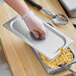 A person in gloves using a Vigor stainless steel slotted pan cover to serve macaroni and cheese.