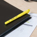 A Bic Brite Liner Fluorescent Yellow pen on a black notebook.