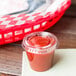 A Solo clear plastic lid on a small cup of red sauce on a table in a food delivery basket.