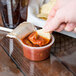 A hand dipping a chip into a small container of Muy Fresco Medium Salsa.