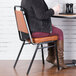 A woman sitting on a Lancaster Table & Seating brown stackable chair with a 2" padded seat at a table.