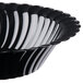 A close up of a black Fineline plastic bowl with a scalloped edge and spiral design.