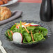 A black Fineline plastic bowl filled with salad with spinach, radishes, and carrots on a table.