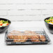 Two Fineline black plastic rectangular trays with food in them on a white table.
