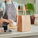 A woman in a grey apron wrapping a brown bag with wooden handles.