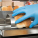 A person wearing blue gloves holding a roll of bread over a counter.