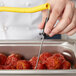 A hand using a Taylor Type-K penetration probe with a yellow coiled cable to measure the temperature of meatballs in a metal container.