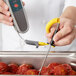 A person using a Taylor Type-K penetration probe to measure meatballs on a yellow flexible cable.