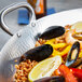An American Metalcraft stainless steel paella pan filled with seafood on a table.