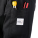 The pocket of a black Mercer Culinary long sleeve chef jacket with a pen and a yellow marker.