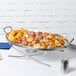 An American Metalcraft stainless steel oval griddle with food on it on a table.