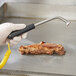 A gloved hand using a Cooper-Atkins Type-K surface probe on a piece of meat.