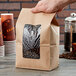 A hand holding a Choice brown kraft paper bag with a window filled with coffee beans.