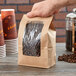 A hand holding a Choice brown Kraft paper bag with a poly window filled with coffee beans.