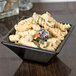 A black GET Siciliano square bowl filled with pasta on a table.