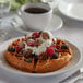 A waffle with berries and whipped cream on a plate.