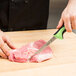 A hand using a Mercer Culinary Millennia Colors narrow boning knife to cut meat on a cutting board.